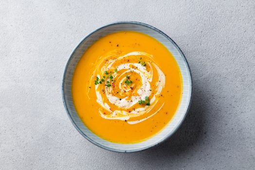 Pumpkin and carrot soup with cream on grey stone background. Top view