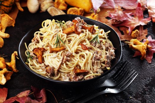 pasta with organic chanterelles. portion of spaghetti pasta with fried chanterelles in a creamy garlic sauce with cheese close-up on a plate on the table.